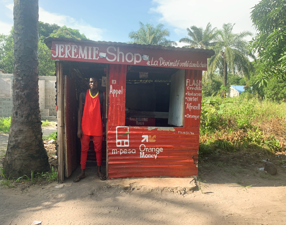 A foto mostra Jeremie na porta de sua loja vermelha que diz "Jeremie Shop"