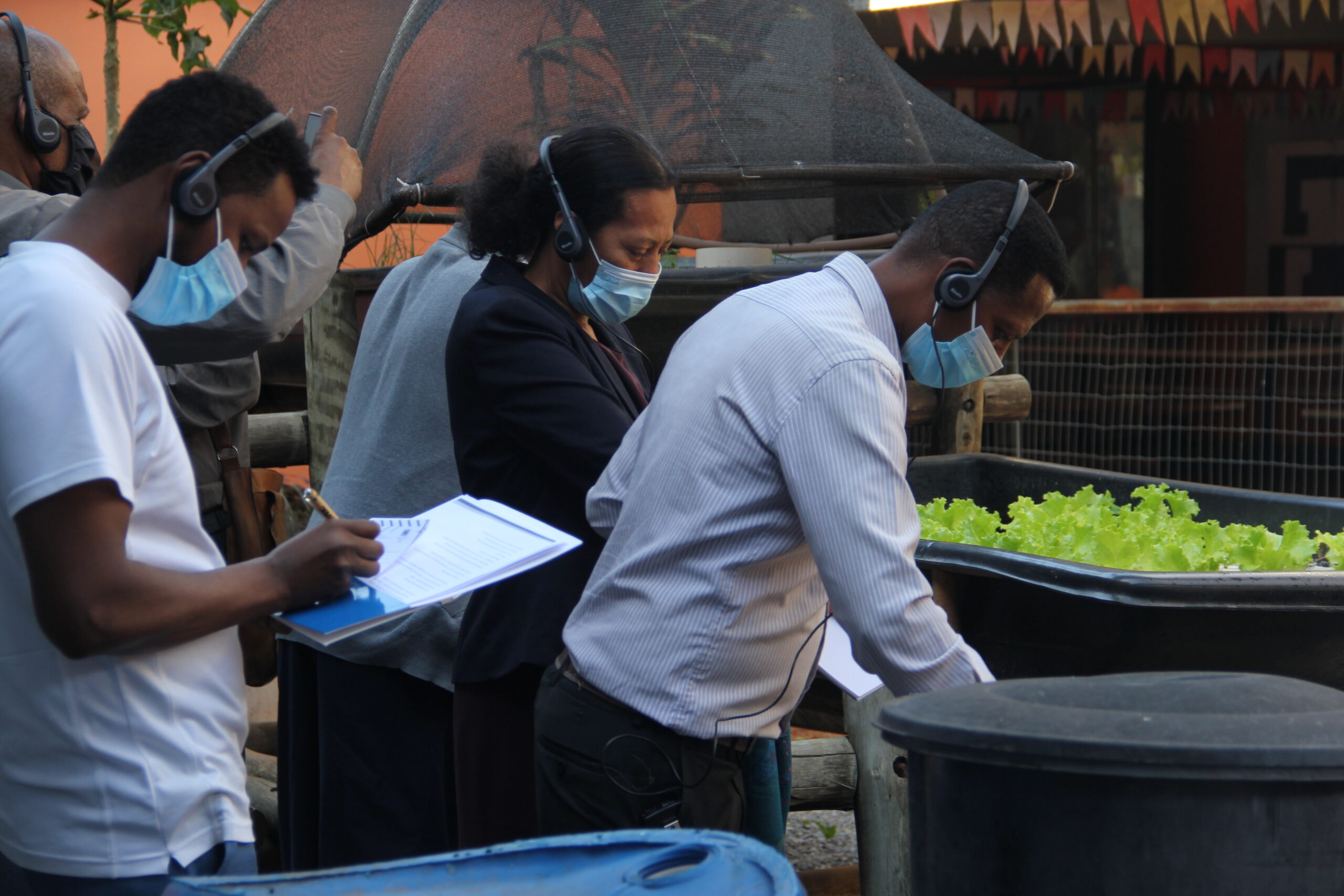Photo showing members of the Ethiopian delegation wearing headsets and masks visiting a public brazilian school in the middle of a community garden.