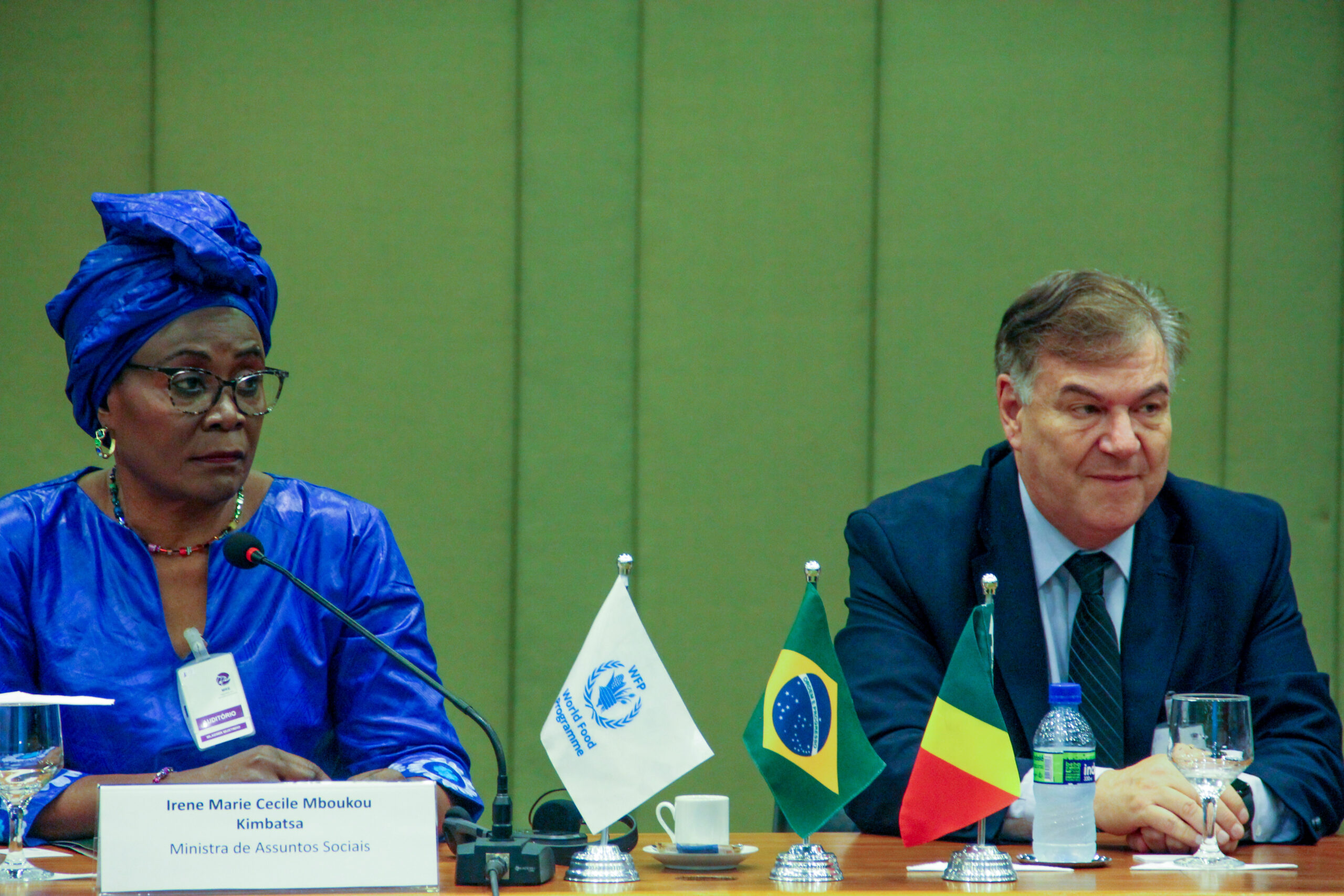 A foto mostra a Ministra de Assuntos Sociais, Irene Marie Cecile Mboukou Kimbtasa, uma mulher negra vestindo uma blusa e um turbante azuis, à esquerda, e o Diretor do Centro de Excelência, Daniel Balaban, um homem branco usando um terno escuro e gravata, à direita.