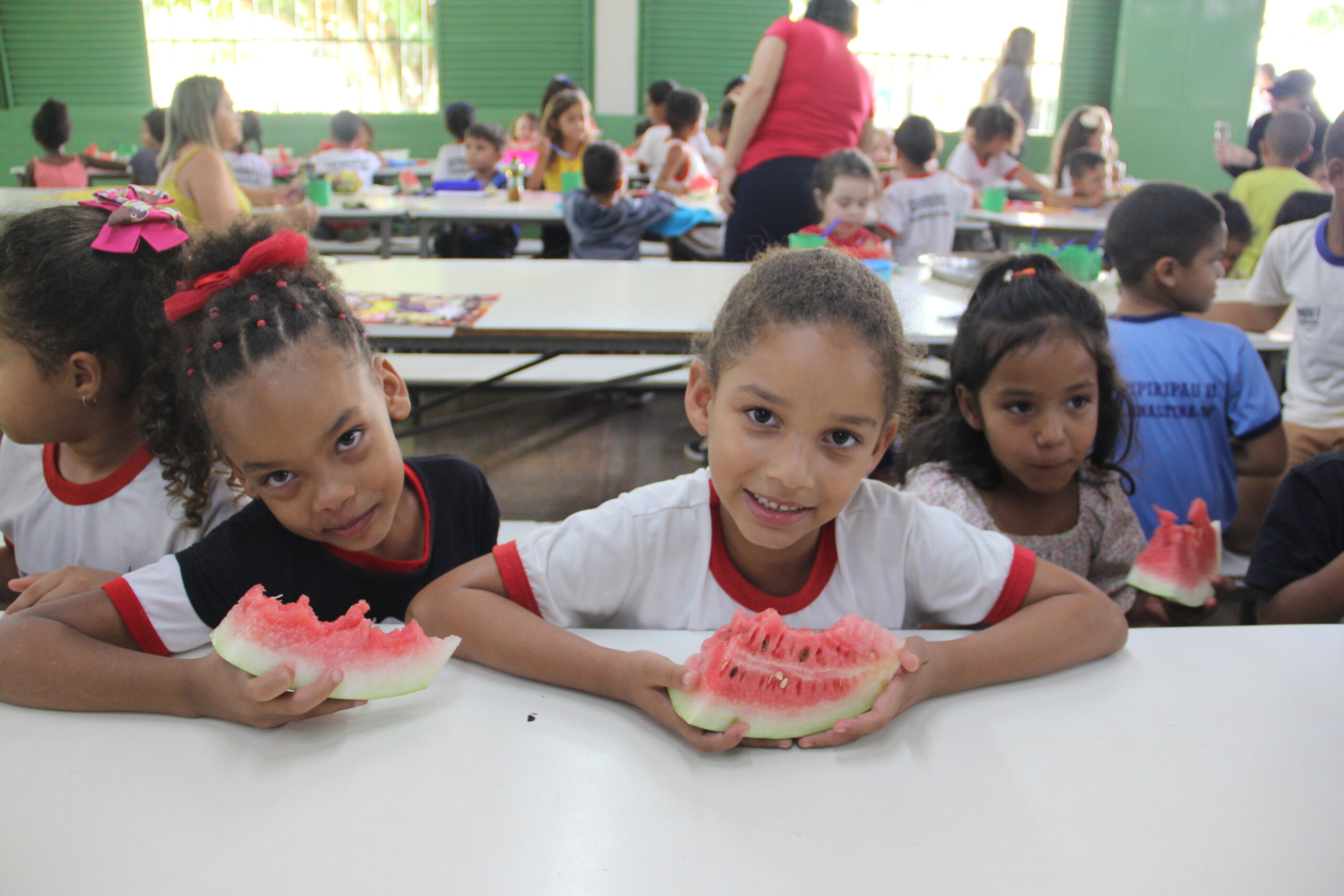 Crianças comendo melancia durante o horário da refeição escolar.
