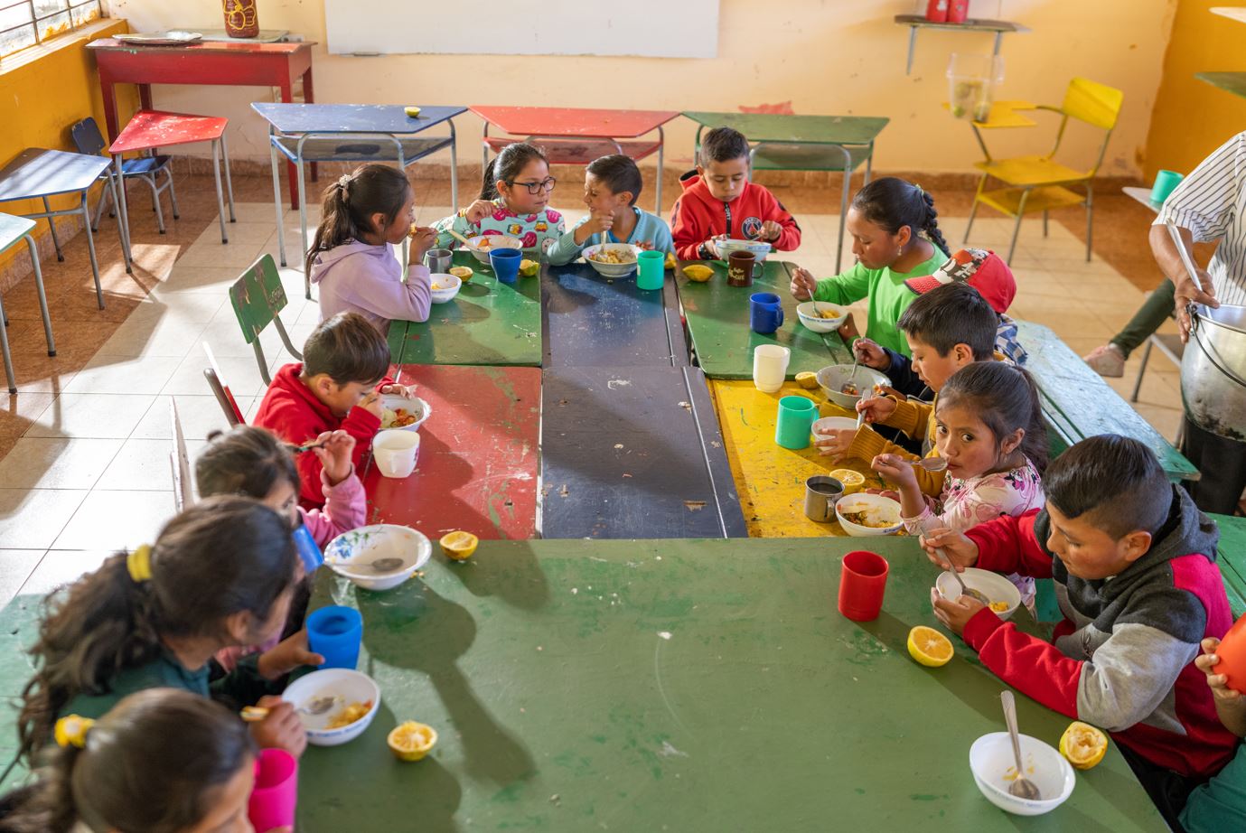 Crianças se sentam em uma mesa de sala de aula para comer o lanche da escola.