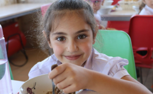 A foto mostra uma menina armenia comendo uma refeição em sua escola.