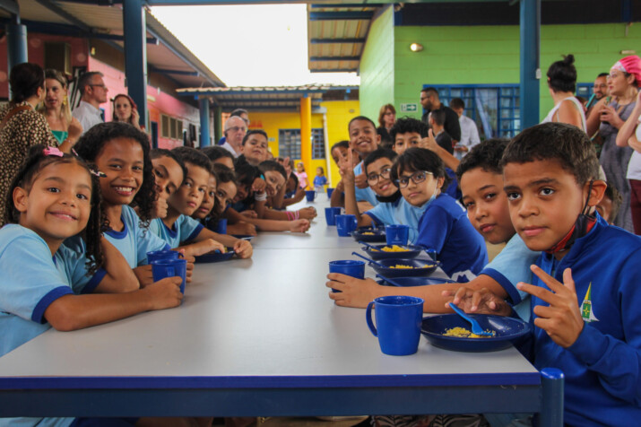 Children in blue uniforms eat their school lunch, consisting of juice and couscous, in a Brazilian public school.