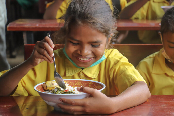 Uma aluna da Escola Filial Básica (EBF) Leilaus, no Timor Leste, desfrutando de sua refeição escolar durante o intervalo do almoço.